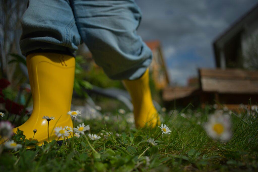 Barn med gule gummistøvler på græsmark med blomster